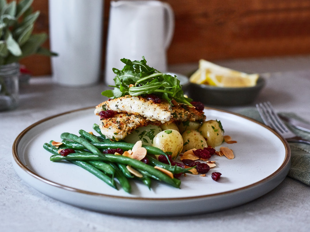 Plated dish with chicken, vegetables, and arugula on a table.