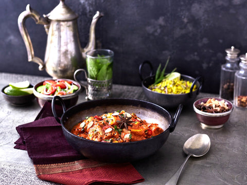 Culinary scene with a bowl of curry, salad, and various accompaniments on a dark surface.