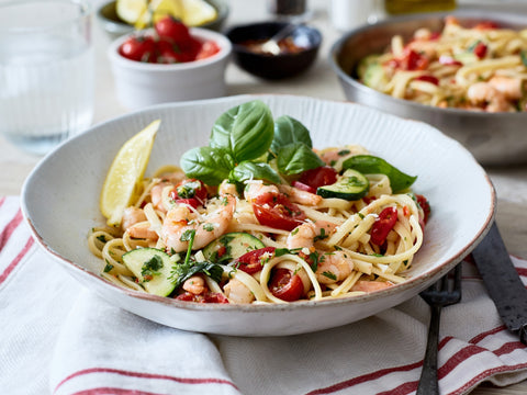 Spaghetti dish with shrimp, tomatoes, and basil in a white bowl on a table.