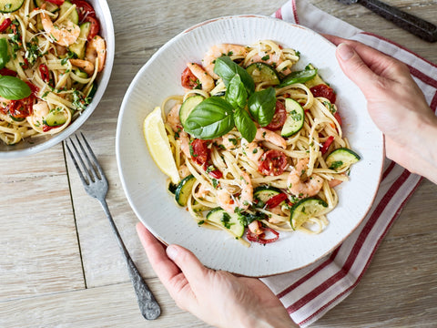 Plate of pasta with vegetables held by a person on a wooden table.