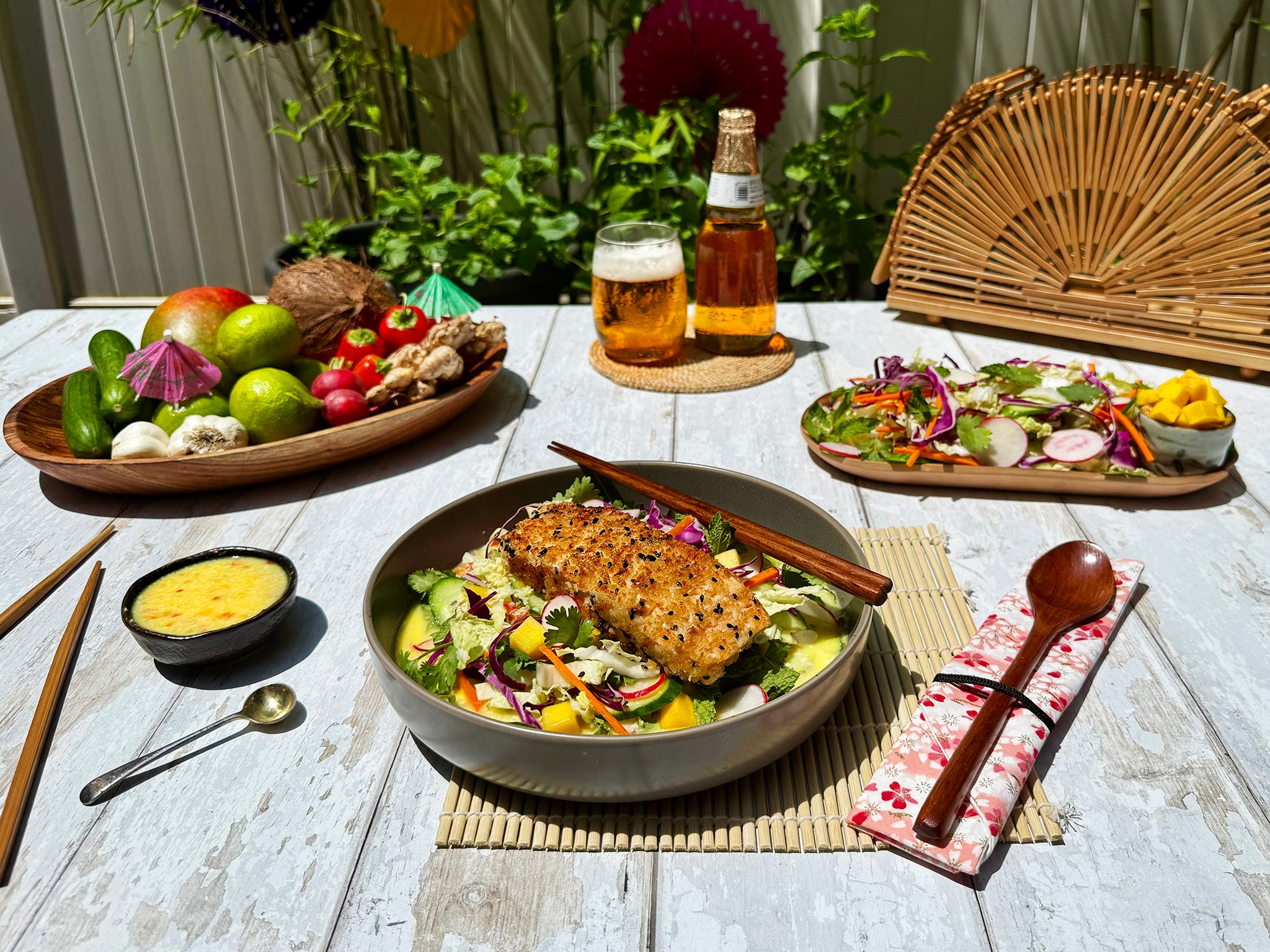 Outdoor setting with a table featuring a salad bowl, plates of vegetables, a bottle of beer, and glasses.