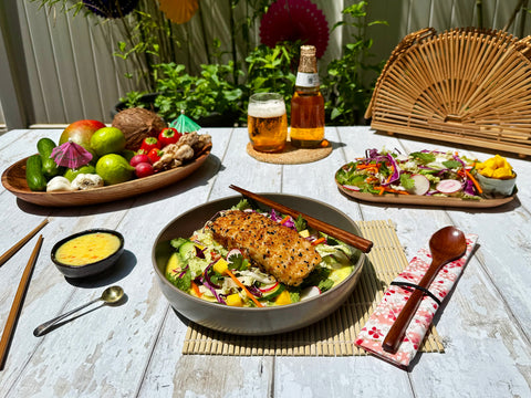 Outdoor setting with a table featuring a salad bowl, plates of vegetables, a bottle of beer, and glasses.