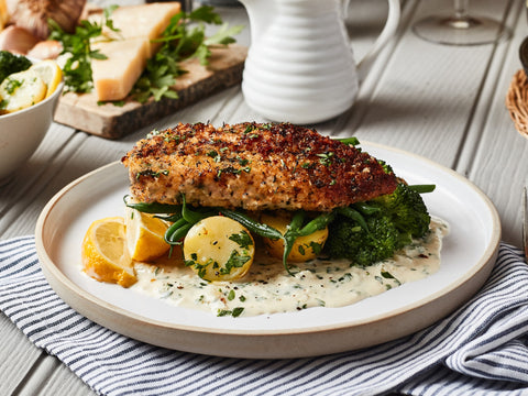 Plated dish of breaded fish with vegetables and lemon on a wooden table.