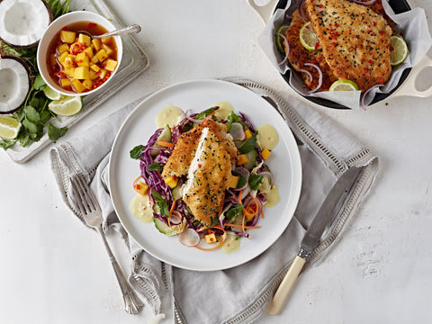 Plated dish of fish with salad on a white table with side dishes.