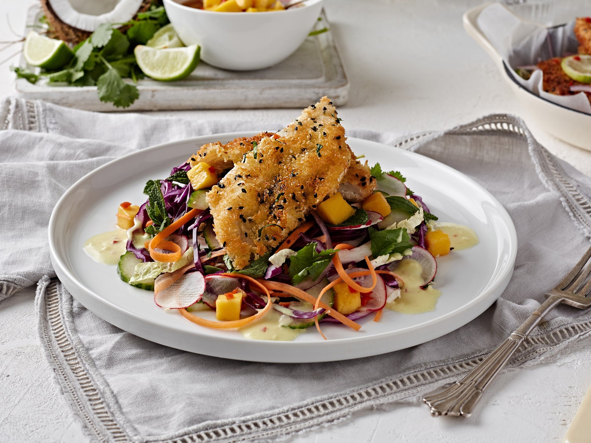 Plated salad with fried fish on a white plate, set on a light gray tablecloth.