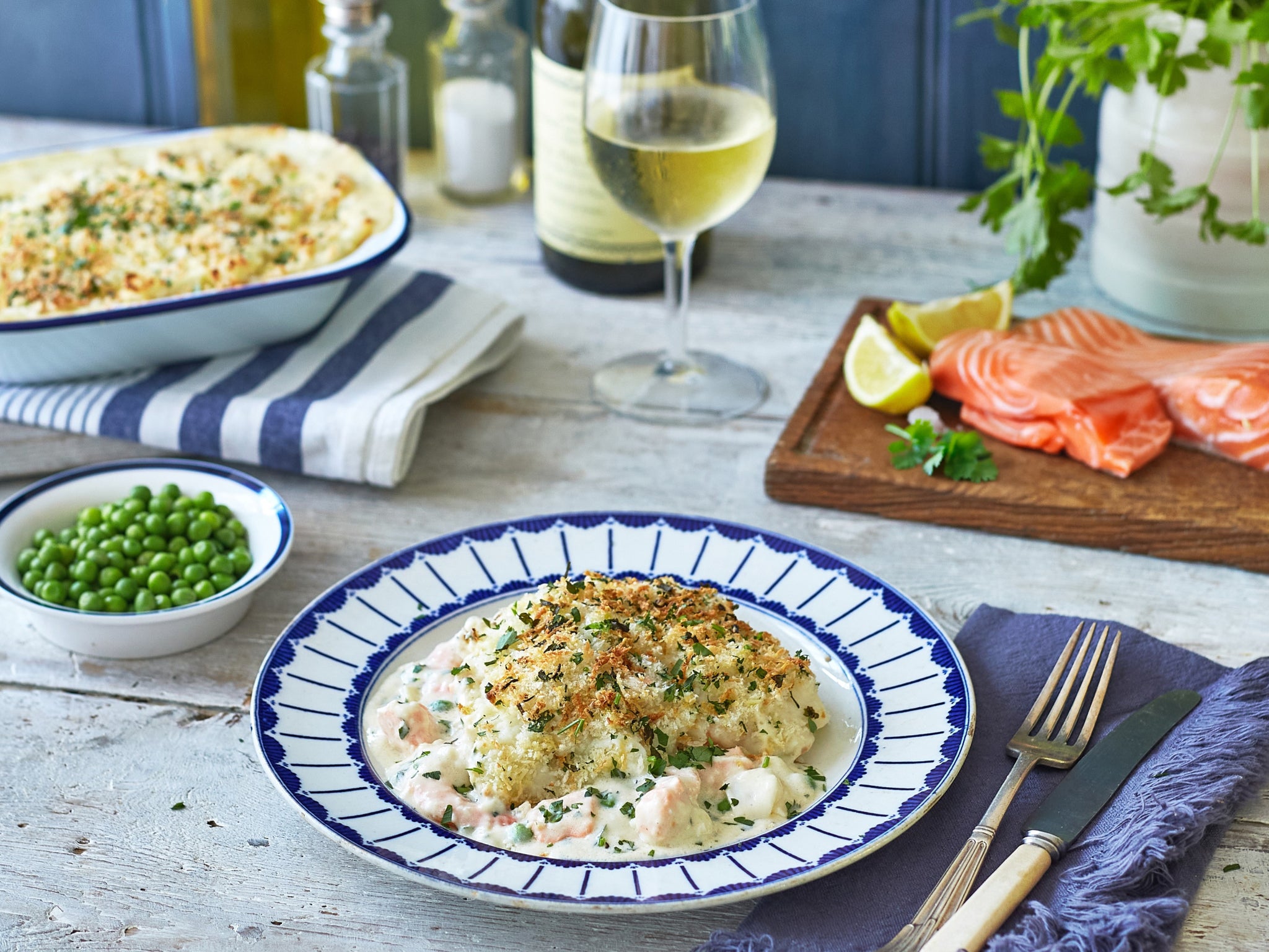 Dinner table with a plate of food, salmon, peas, and a glass of white wine.
