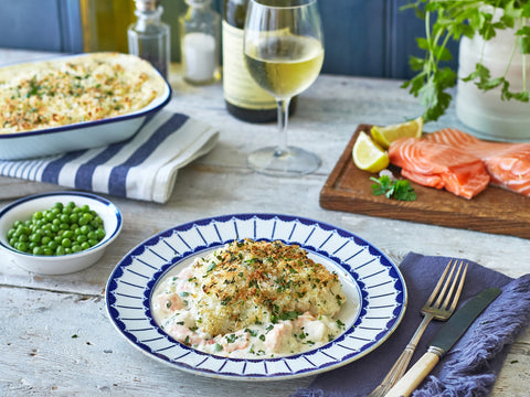 Dinner table with a plate of food, salmon, peas, and a glass of white wine.