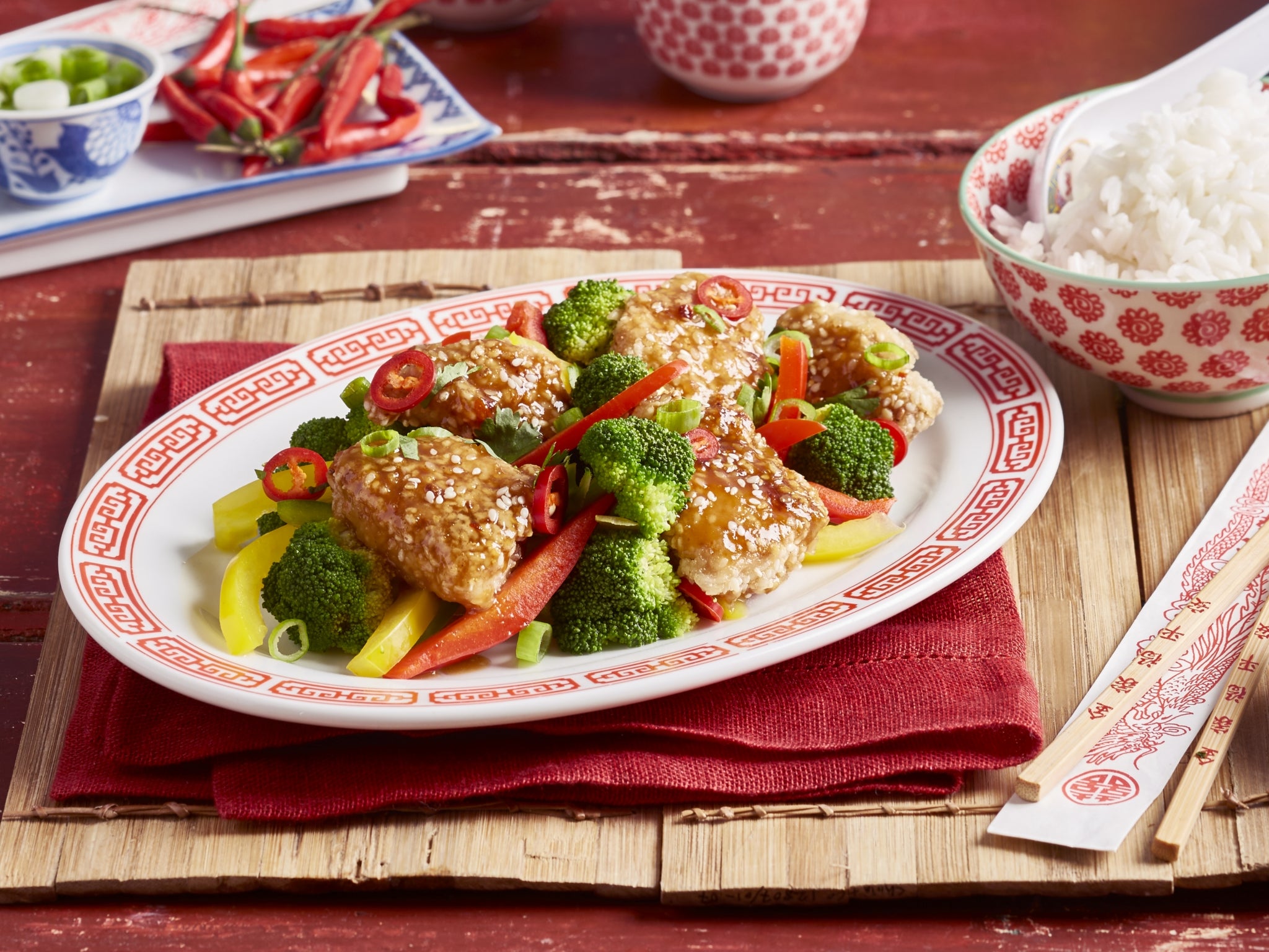 Plated dish of chicken and vegetables on a wooden table with red and white patterned plates.