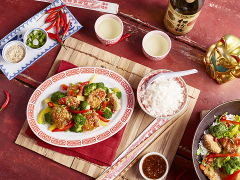 Chinese dish with vegetables and rice on a red tablecloth with chopsticks and sauces.