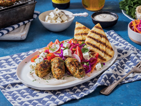 Plated dish with falafel, vegetables, and grilled bread on a blue tablecloth.