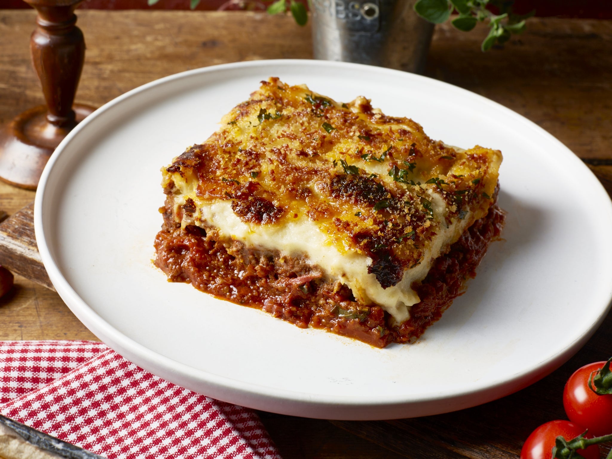 Slice of lasagna on a white plate with a wooden table background