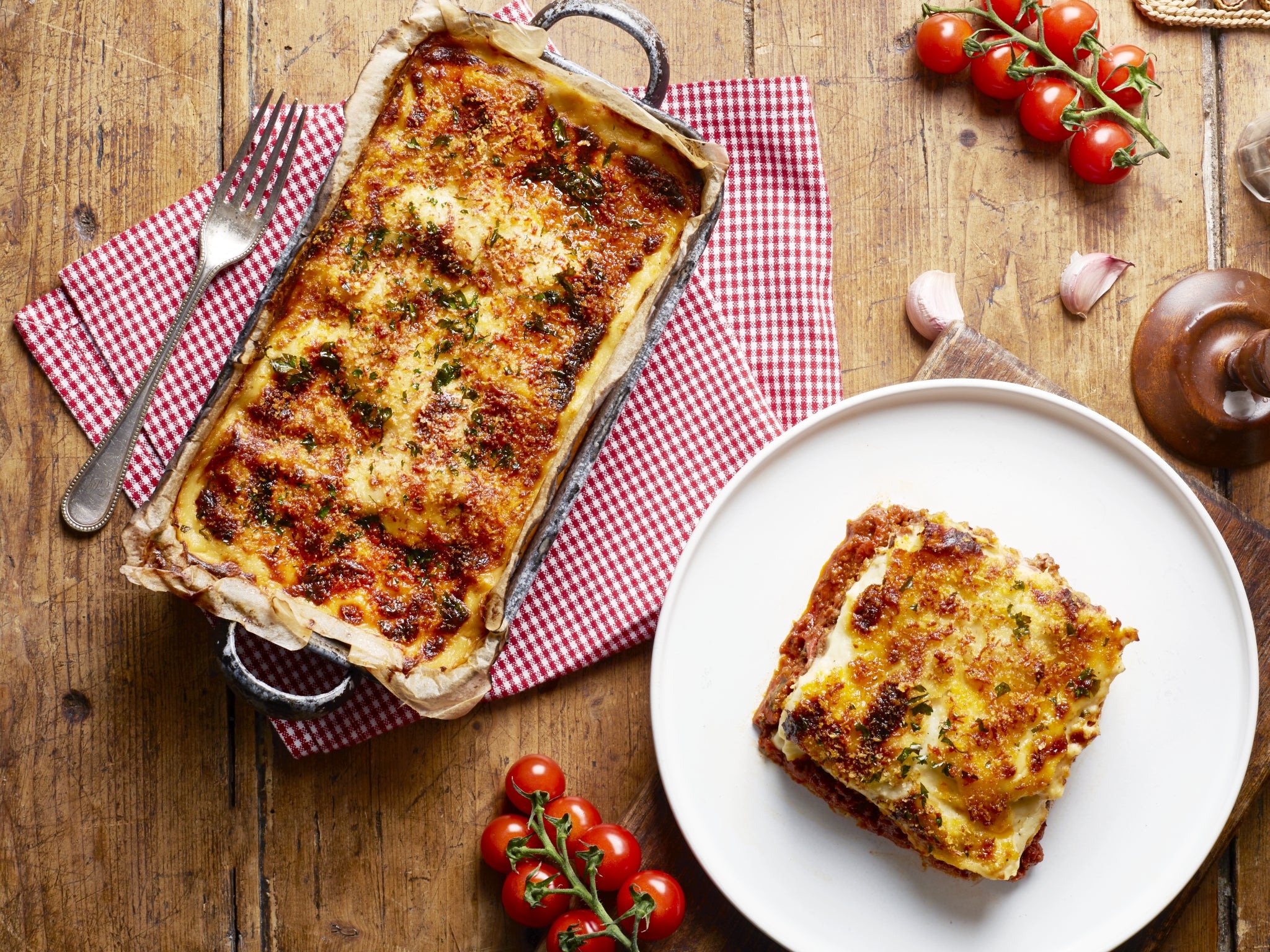 Baked lasagna with a slice on a plate on a wooden table.