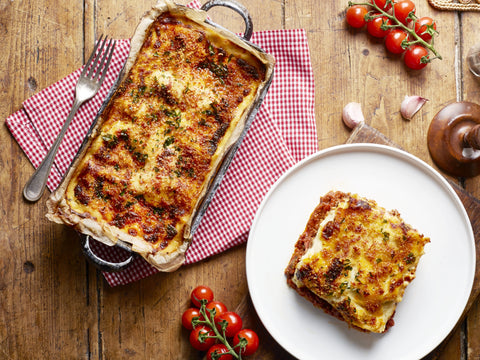 Baked lasagna with a slice on a plate on a wooden table.