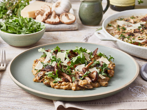 Plate of mushroom risotto with arugula on a wooden table with side dishes.