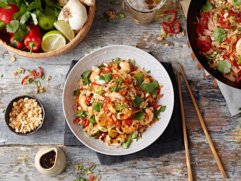 Plated dish of noodles with vegetables on a wooden table with ingredients and utensils.
