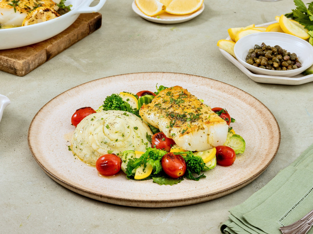 Plated dish with fish, vegetables, and mashed potatoes on a light surface.