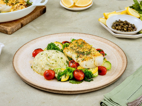 Plated dish with fish, vegetables, and mashed potatoes on a light surface.