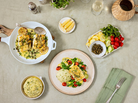 Dinner table set with plates of food, including fish dishes and vegetables, on a light background.