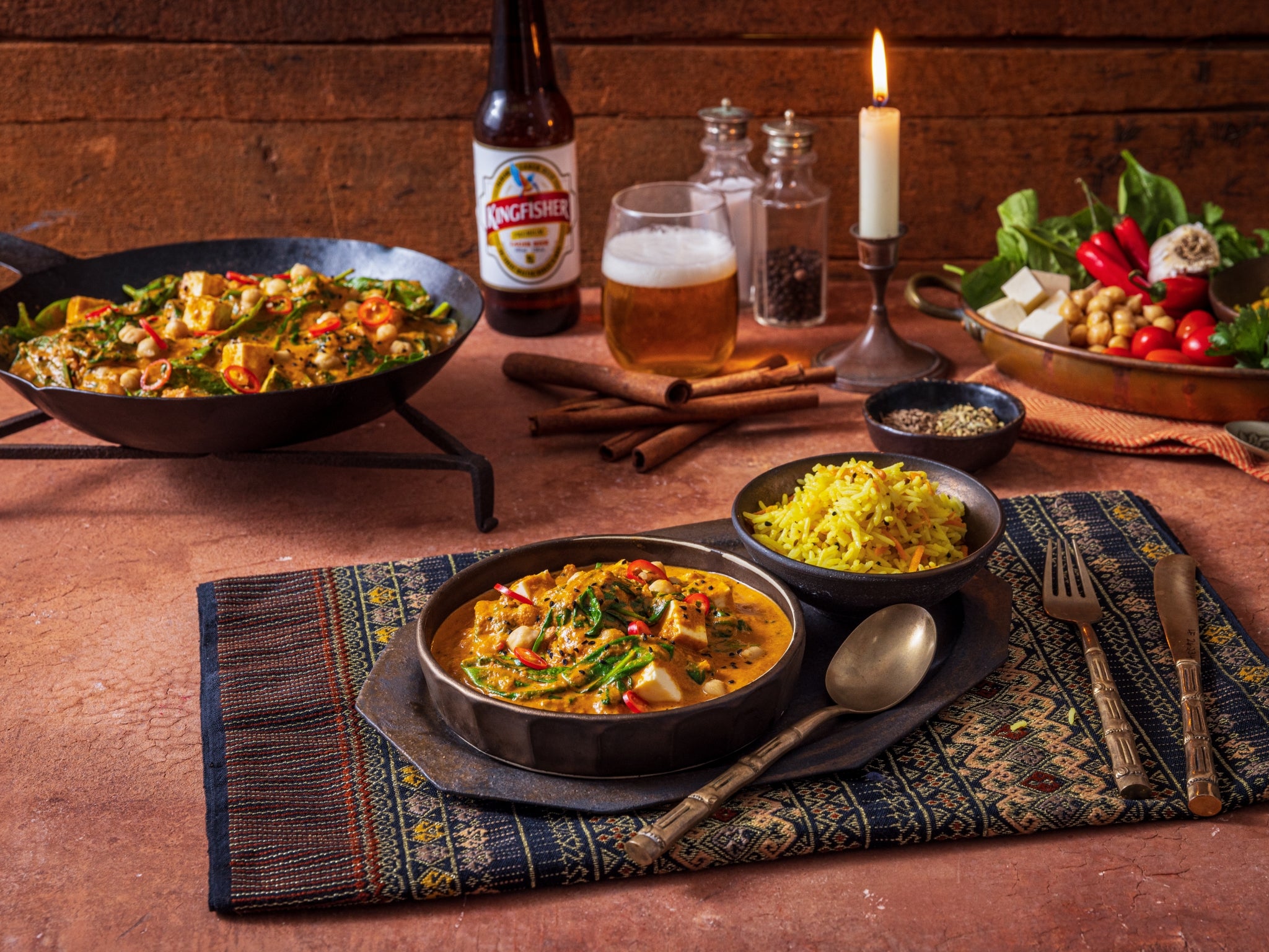 Dinner table with Indian food, beer, and candles on a wooden background