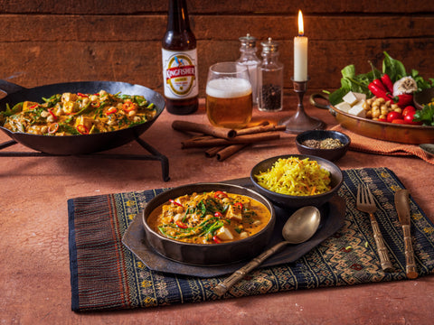 Dinner table with Indian food, beer, and candles on a wooden background