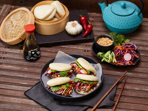 Dishes of food on a wooden table with a blue teapot and various condiments.