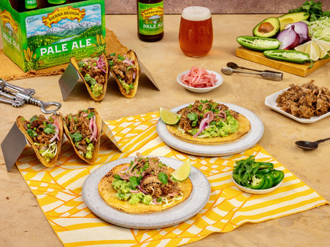 Table with tacos, beer, and sides on a wooden surface