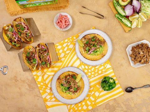 Tacos on a yellow patterned napkin with various taco ingredients on a wooden surface.