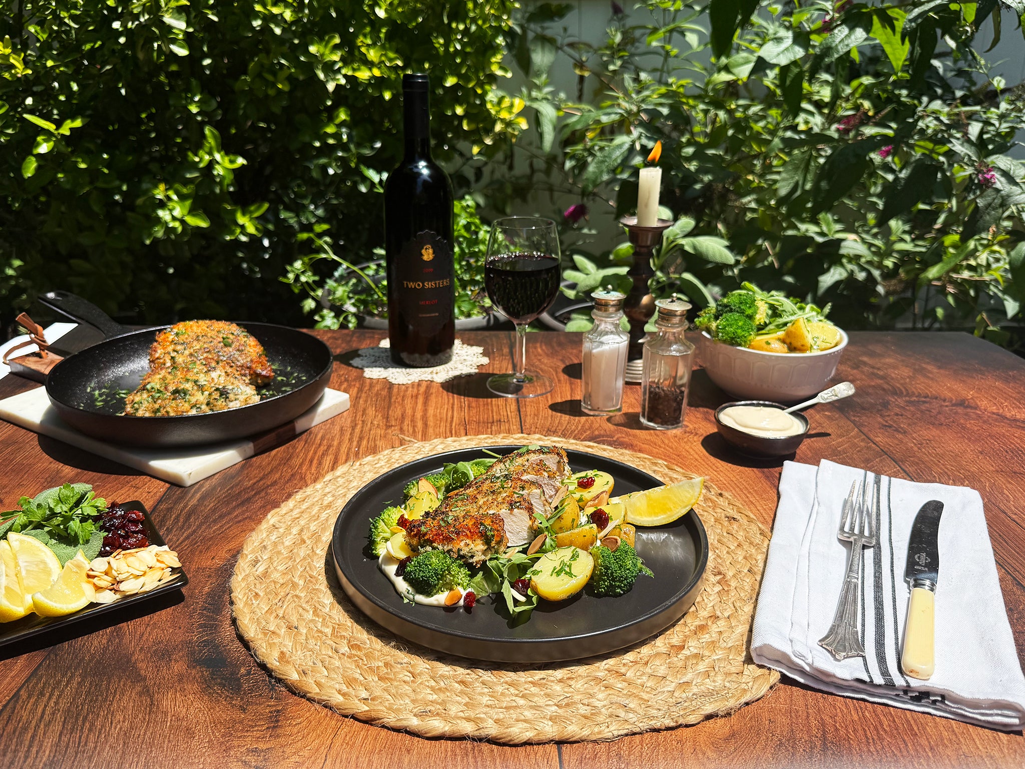 Dining table set with a meal, wine, and cutlery outdoors.