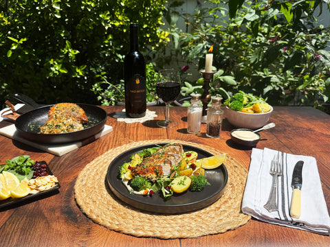 Dining table set with a meal, wine, and cutlery outdoors.