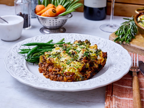 Plated dish of meatloaf with green beans on a white plate, set on a table with a wine bottle and glasses.