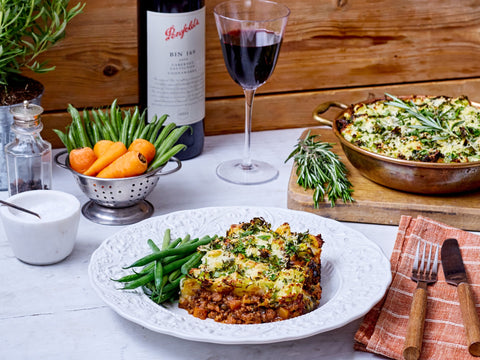 Dinner setting with lasagna, green beans, carrots, and a glass of red wine on a wooden table.