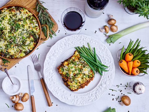 Plated dish with green beans and carrots, surrounded by ingredients on a white surface