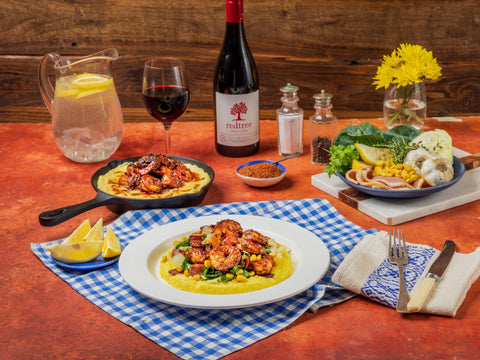 Dinner table set with polenta, chicken, lemon wedges, wine, and flowers.
