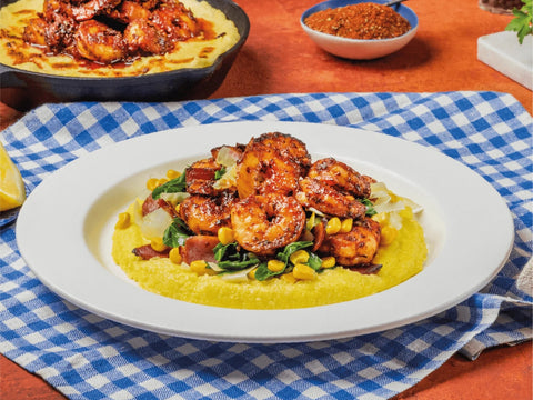 Shrimp and grits dish on a white plate with a blue checkered tablecloth