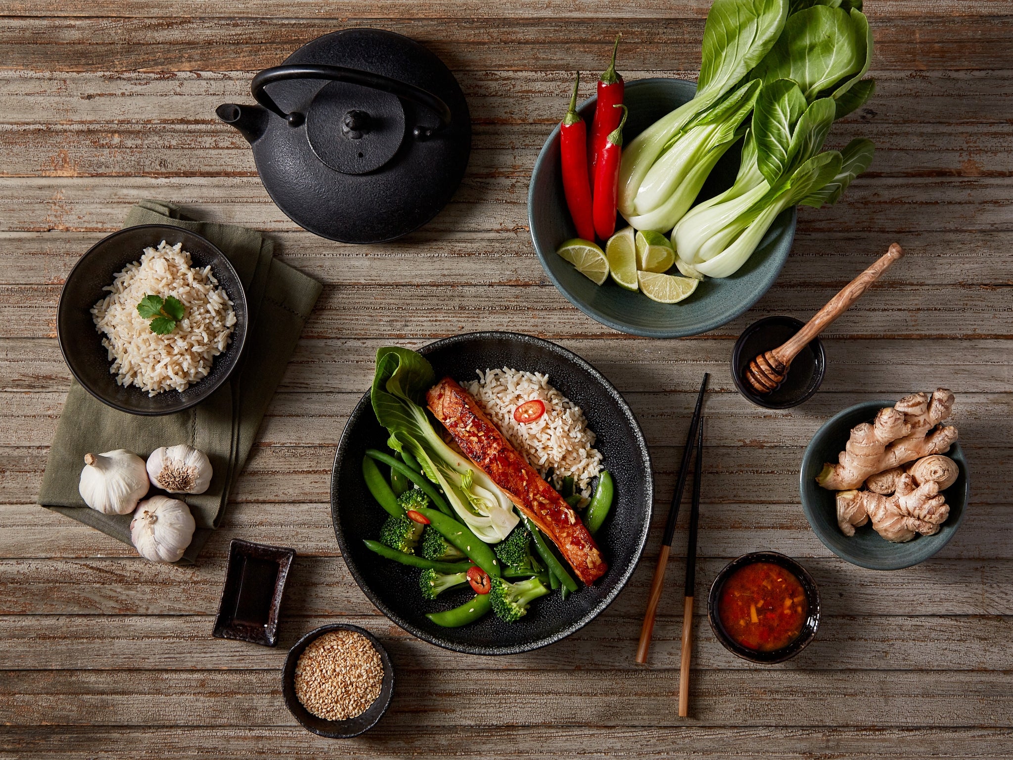 Dinner setup with rice, vegetables, and a teapot on a wooden table.
