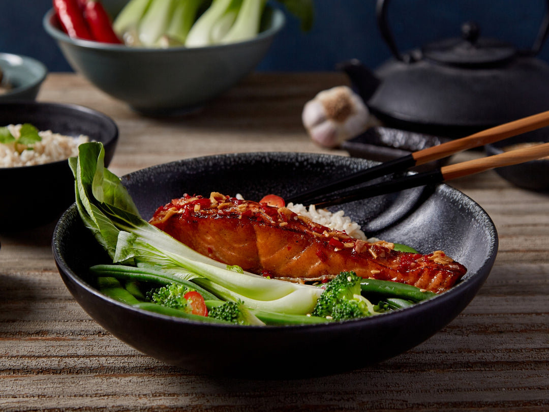 Bowl of food with salmon, vegetables, and rice on a wooden table.
