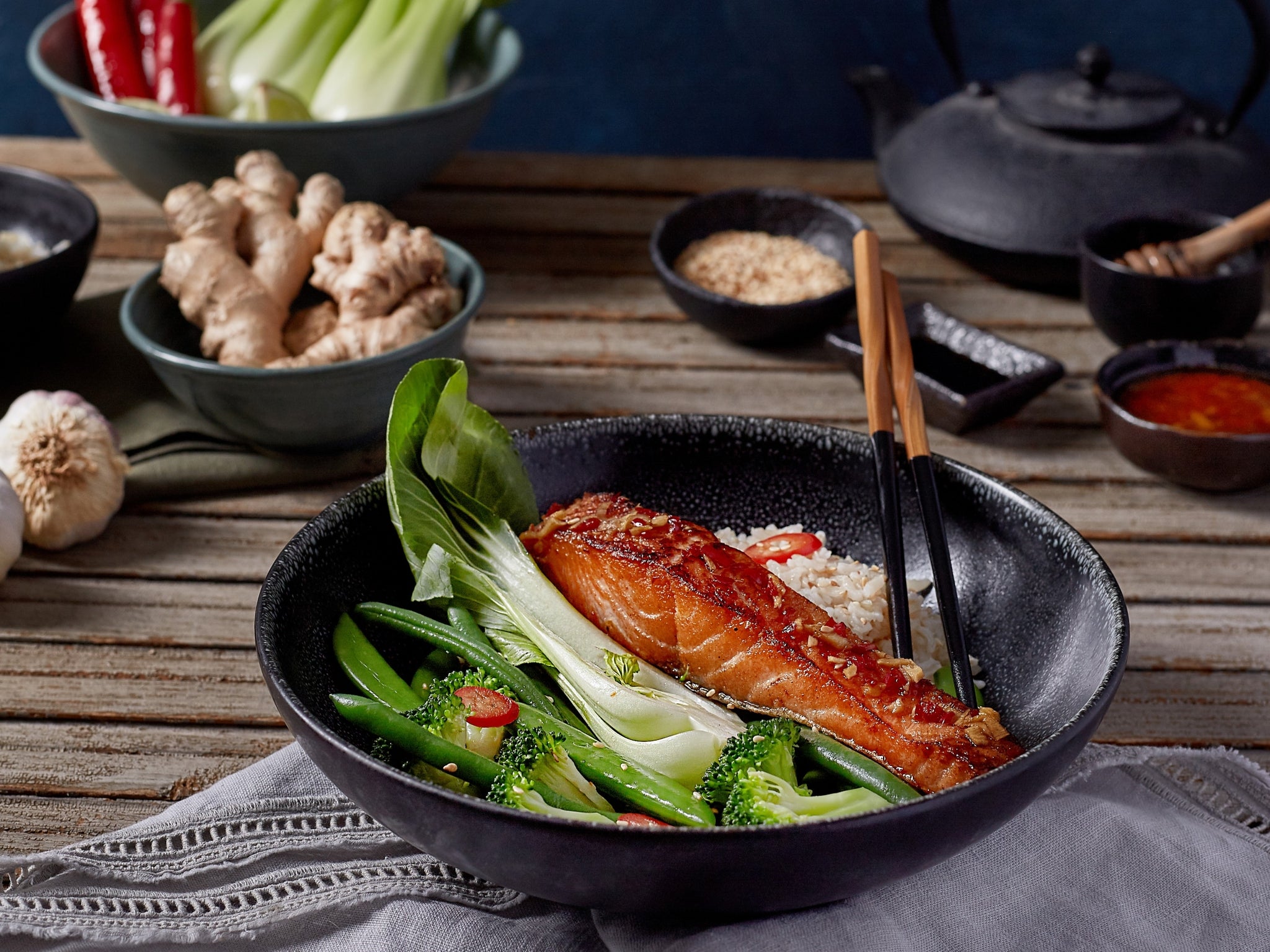 Bowl of salmon with vegetables on a wooden table with various seasonings.