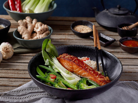 Bowl of salmon with vegetables on a wooden table with various seasonings.