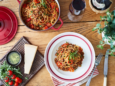 Spaghetti dish on a wooden table with a plate, fork, and wine bottle.