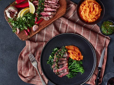 Dinner setup with steak, vegetables, and sweet potato on a black plate with a side of salad.