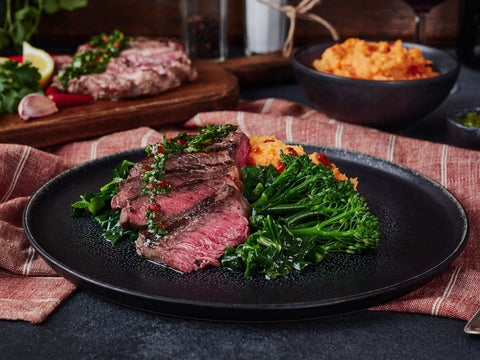 Steak with greens on a black plate with a red checkered tablecloth