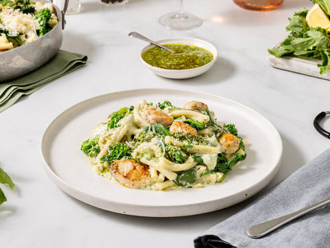 Plate of pasta with shrimp and greens on a white table with side dishes.