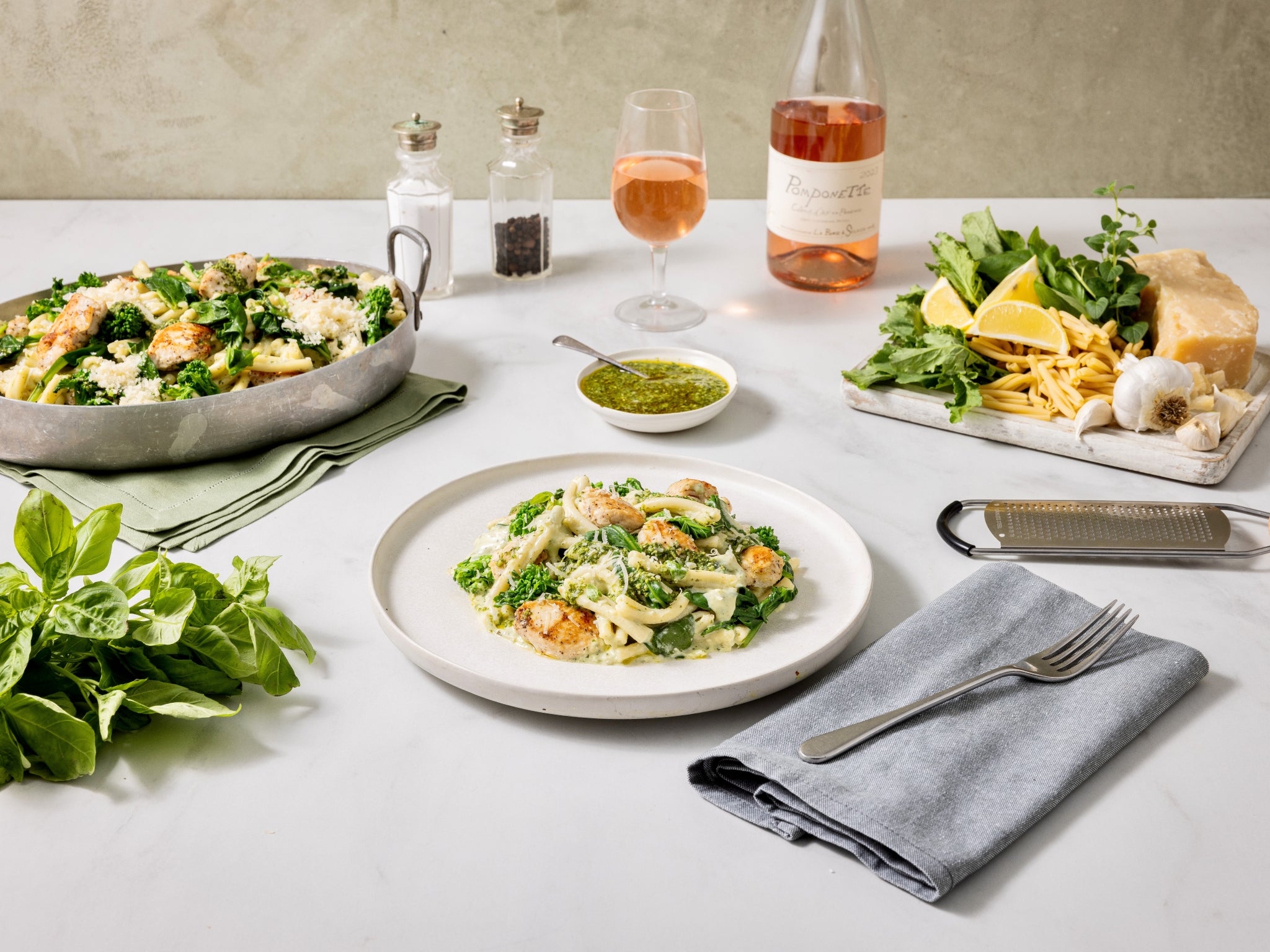 Dinner table set with pasta dish, salad, and wine on a neutral background