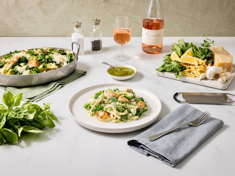 Dinner table set with pasta dish, salad, and wine on a neutral background