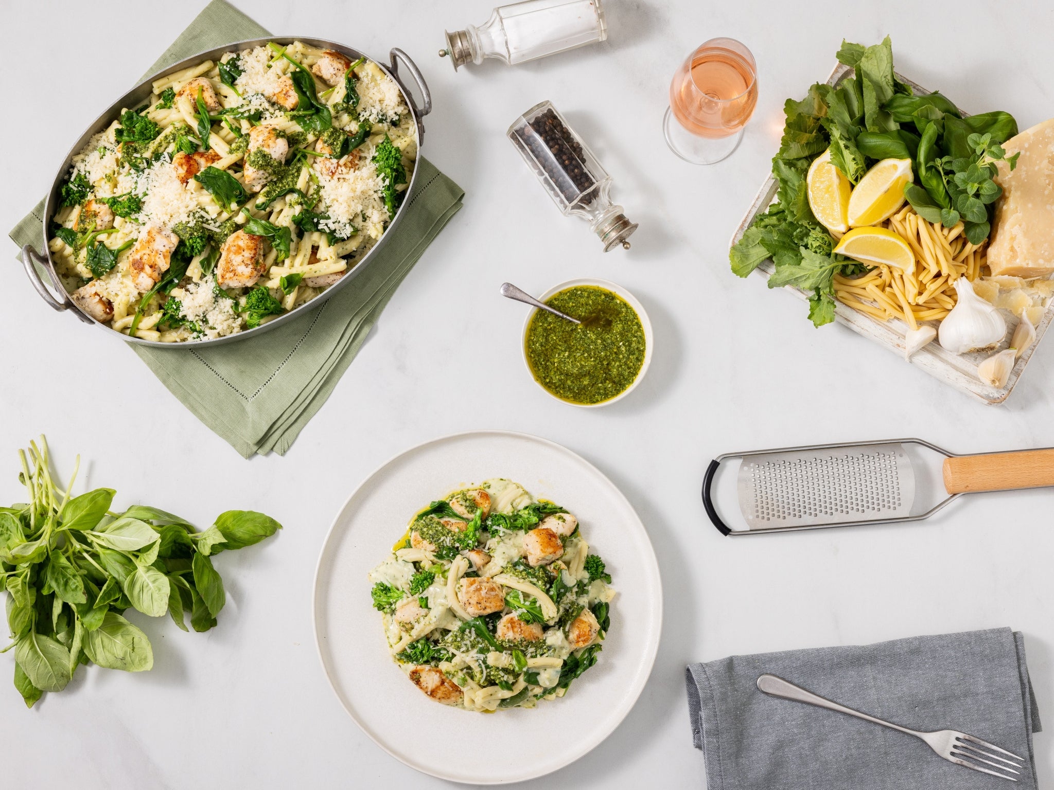 Pasta dish with greens and a side of salad on a white table.