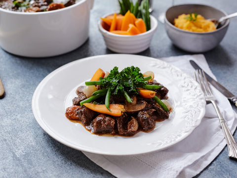 Plated dish of beef with vegetables on a gray surface with additional dishes in the background.