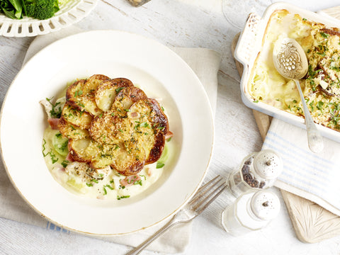 Dish of roasted cauliflower with a side of mashed potatoes on a white tablecloth.