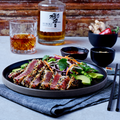 Plated dish of tuna salad with a glass of whiskey and bottle in the background.