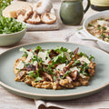Plate of mushroom risotto with arugula on a wooden table with side dishes.