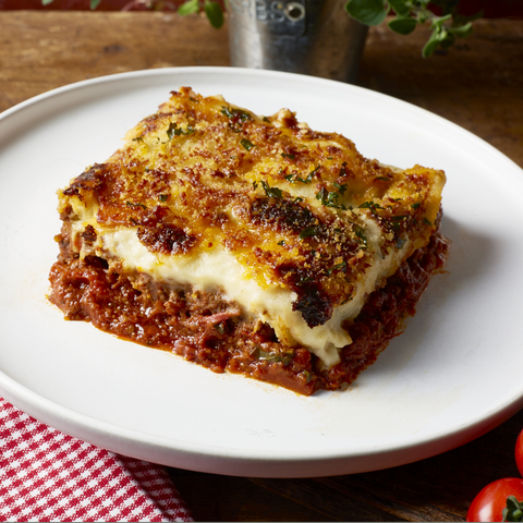 Slice of lasagna on a white plate with a wooden background